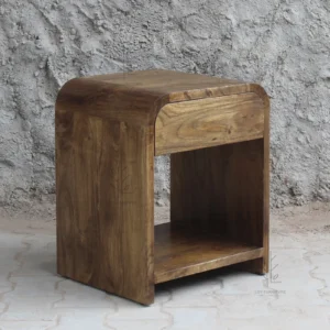 Siguiendo la línea orgánica de la colección Ibiza, esta mesita de noche en madera de mango color nogal destaca por sus formas redondeadas.